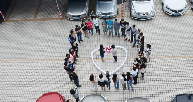 Chinese macht seiner Freundin einen Heiratsantrag in einem Herzen aus 99 iPhones, umgeben von Freunden