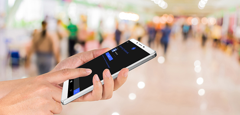 male hand is holding a modern touch screen phone and Blurred image of people walking at shopping mall , blur background with bokeh